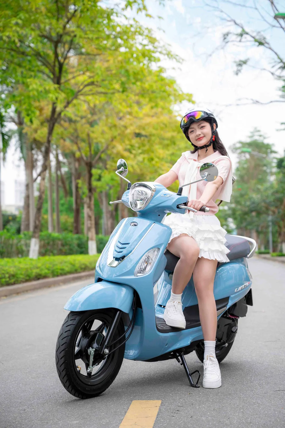Cô gái đội mũ bảo hiểm chạy xe tay ga trên phố rợp cây