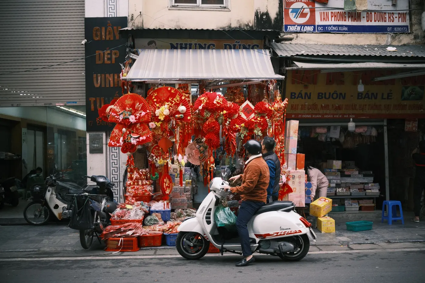 Hai người đi xe tay ga qua dãy hàng trang trí Tết trên phố